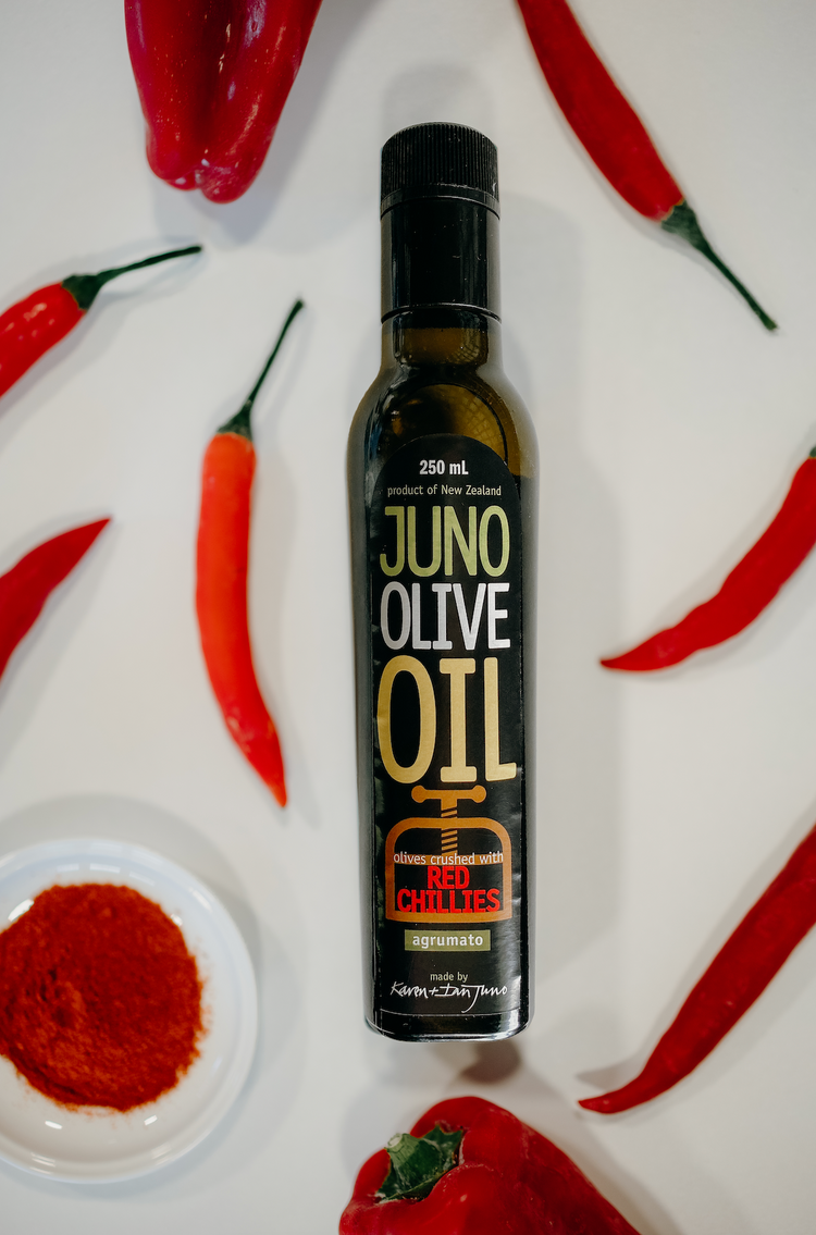 250 mL dark green bottle of Red chilli agrumato oil, surrounded by red chillies.