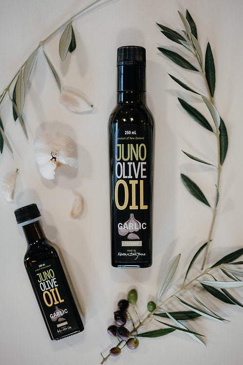 100 and 250 mL dark green bottles of Garlic Infused Olive oil. Garlic and Olive leaves surrounding