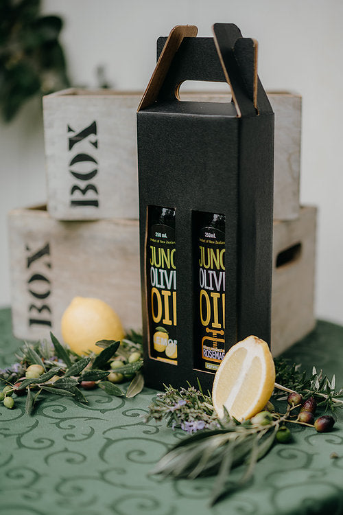 Two 250 mL dark green bottles of olive oil in a black gift box, with olives and fruit surrounding.